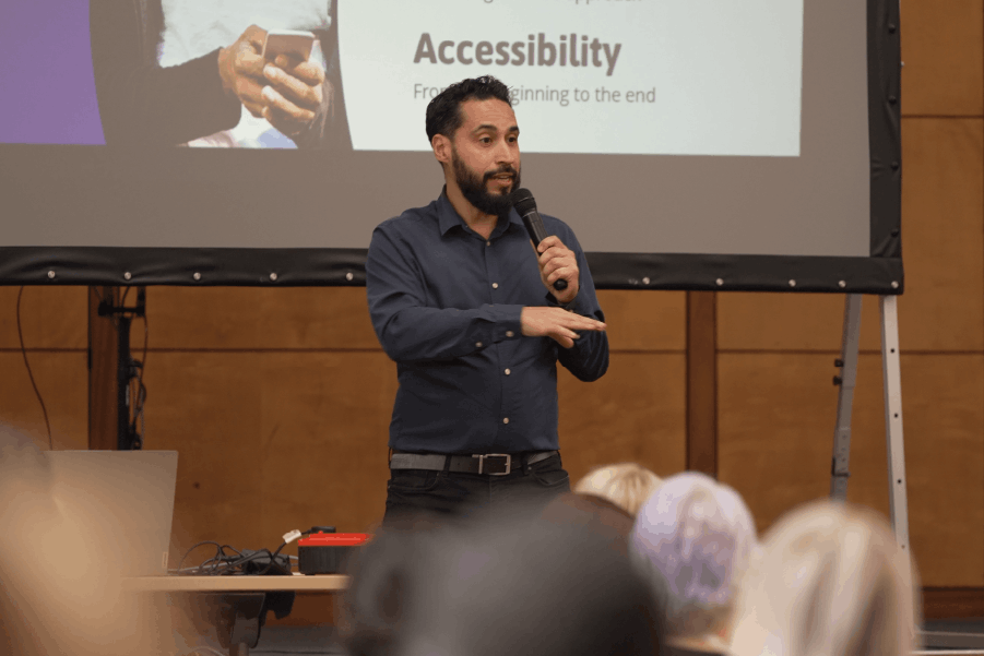 Passion4Social’s Managing Director, Thiago, speaking animatedly into a microphone with the bottom half of a projector screen in the background and a crowd of people in the audience.